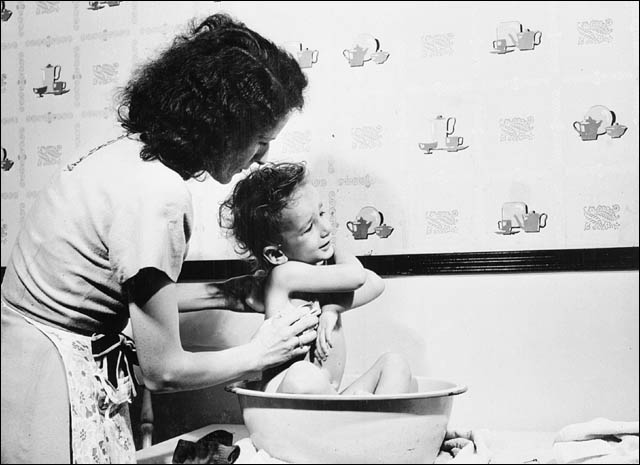 Mme William Meadows de Hull en train de baigner Gary, trois ans, dans la cuisine de leur appartement de quatre pièces