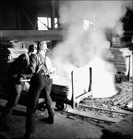 Des ouvriers jettent une feuille de zinc électrolytique dans une fournaise de fusion à la fonderie Consolidated Mining and Smelting Company of Canada Ltd