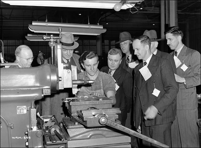 Rédacteurs d'un hebdomadaire observant un machiniste à l'usine Otis Fenson